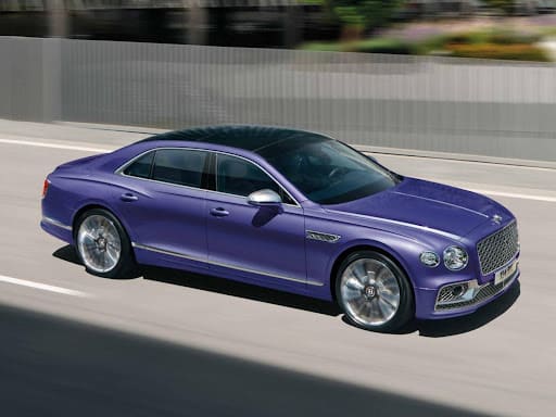 A purple bentley flying spur driving on a highway.