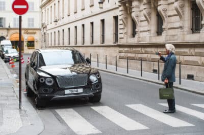 Man taking a picture of Bentley Bentayga parked on the street