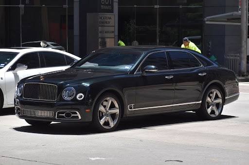 A portrait of a black Bentley Mulsanne luxury sedan cruising in a downtown district