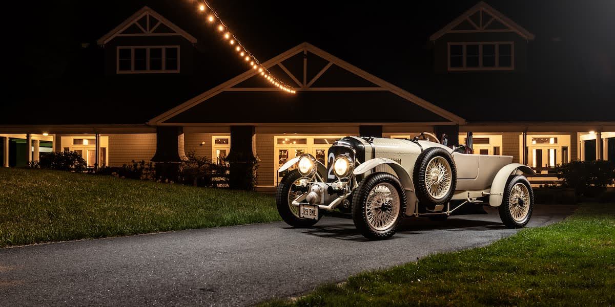 Vintage Bentley car parked under string lights at night with clear view of bentley logo on grille, symbolizing classic car logo with wings.