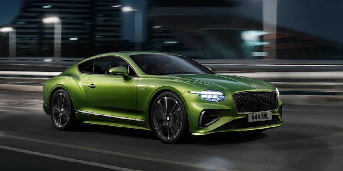 Green Bentley Continental GT Speed Hybrid driving at night on a city bridge, showcasing luxury coupe design and hybrid performance.